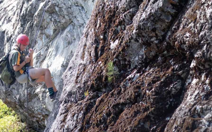 a person looks down as they take a break from rock climbing on an outward bound course